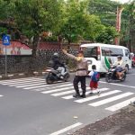 Bhabinkamtibmas Kelurahan Gianyar Rutin Menolong Anak Anak Sekolah Menyebrangi Jalan.