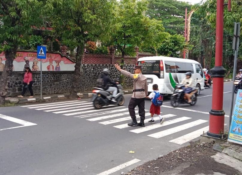 Bhabinkamtibmas Kelurahan Gianyar Rutin Menolong Anak Anak Sekolah Menyebrangi Jalan.